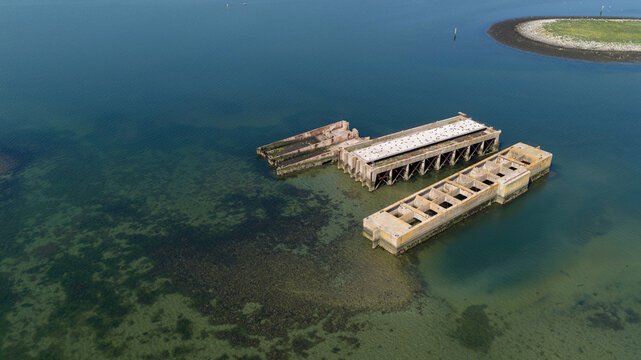 Aerial view of the historic concrete caissons at Inlaag Schelphoek, remnants of the 1953 flood defense, resting in the clear coastal waters of Serooskerke Schouwen, Zeeland, Netherlands.