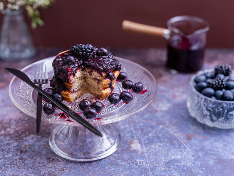 Close-up of fluffy pancakes with berry compote and fresh berries served on an elegant glass cake stand