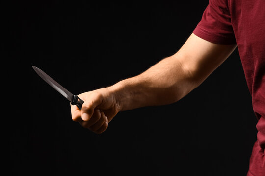 Violence and aggression concept, man holding a sharp kitchen knife in a threatening gesture, crime and danger theme on a dark background