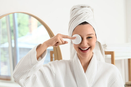 Skincare routine and self care, happy woman with towel on head using cotton pad for facial cleansing in bright bathroom for morning beauty treatment