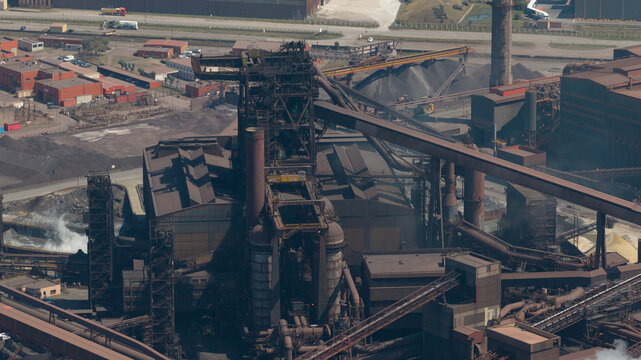 Aerial view of the ArcelorMittal steel plant featuring large blast furnaces, complex conveyor systems, and industrial storage piles in Dunkerque, Hauts-de-France, France.