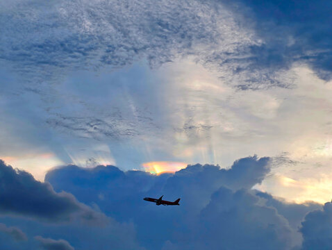 Silhouetted airplane flies through dramatic clouds with sunbeams piercing through the sky at twilight