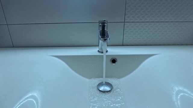 Running water from chrome faucet into bathroom sink with natural water sound