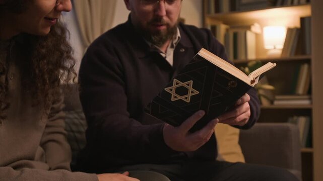 Middle aged Caucasian man reading Jewish prayer book aloud to relative at home during Hanukkah. Ideal for holiday marketing, religious campaigns, and cultural projects