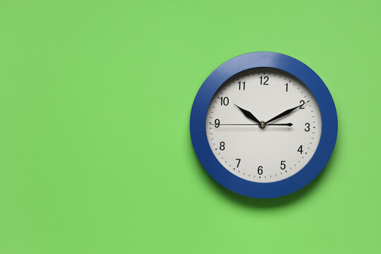 Time management and deadline pressure, blue wall clock on a green background showing ten past ten for business efficiency and punctuality concepts
