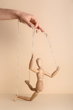 Manipulation and control concept hand holding strings of a wooden mannequin puppet to show influence power dynamics and lack of personal agency