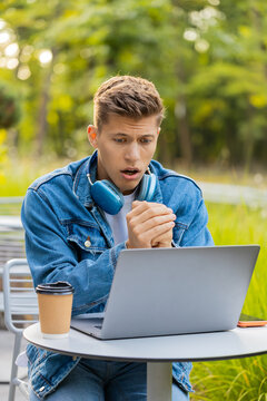 Young man facing laptop failure and problem in city street with fear shock and frustration after bad result. Adult guy tourist working outdoors feels upset tired and worried after unexpected setback.