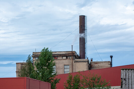Industrial factory building with tall chimney smoke stack under cloudy blue sky.