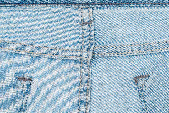 Closeup of light blue denim fabric showing detailed stitching, texture, worn areas. Soft natural lighting highlights weave pattern subtle fading