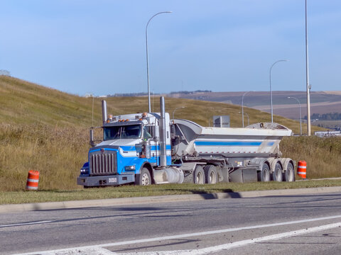 Calgary, AB, Canada. Oct 2, 2026. A blue and white semi dump truck parked along a grassy highway shoulder on a sunny day.