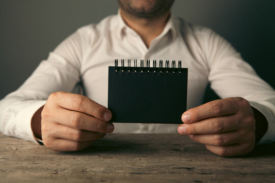 Businessman holding a black notepad on a dark background.