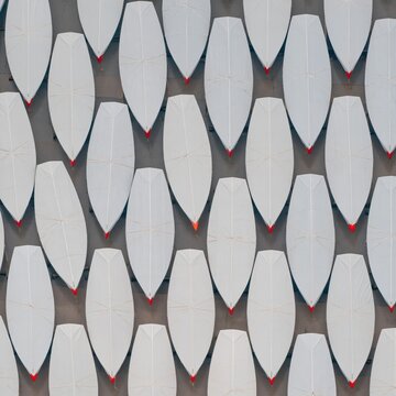 Shrink-wrapped boat hulls in a symmetrical pattern, featuring wet grey asphalt and red keels for maritime and industrial backgrounds