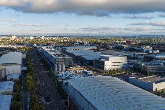 Aerial view of a modern data center complex with rooftop cooling units situated next to railway tracks and surrounded by industrial warehouses in the United Kingdom.