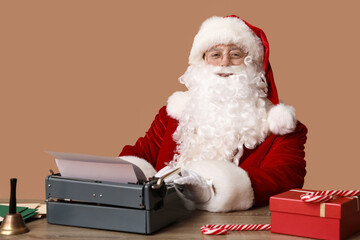 Obraz premium Santa Claus with vintage typewriter, gift box, candy canes and jingle bell at table on brown background