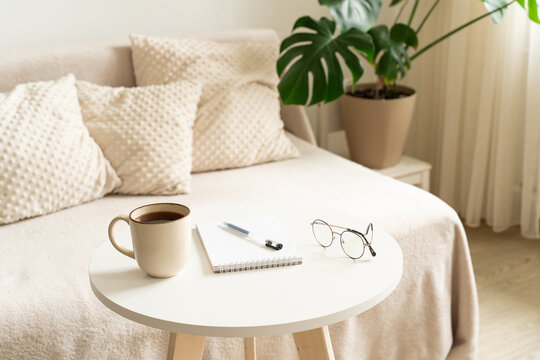 Home interior, an atmosphere of coziness and relaxed pace of life, cup of coffee, notebook, pen, and glasses on table in light-filled room. Mindfulness, journaling, me-time, and calm daily routine
