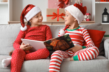Obraz premium Cute happy little children dressed as elves reading book on Christmas at home
