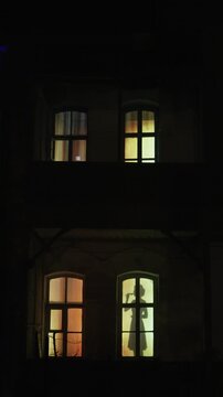 The silhouette of a lonely young woman with a glass of wine in the window of a house at night