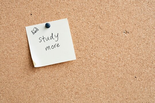 Sticky note with study more handwritten goal pinned to a textured cork board, featuring a matte push pin for planning and motivation