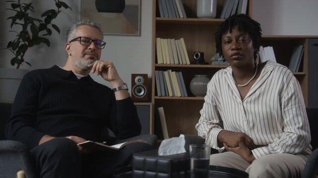 Portrait of middle aged Caucasian psychologist and young adult African American female client looking into camera during therapy session. Footage suited for mental health counseling services