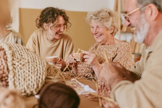 Seniors learning knitting with a tutor at a community center table, a cozy scene of togetherness for active aging and hobby classes