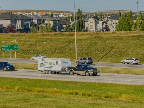 Calgary, AB, Canada. Oct 2, 2026. A pickup truck towing a travel trailer driving on a multi-lane highway past suburban homes.