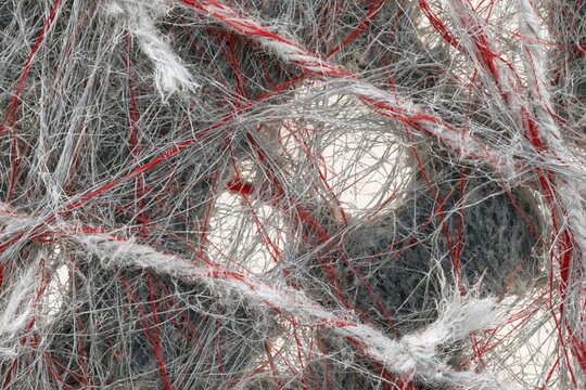 Tangled fibers and textile mesh with red and grey strands, featuring a coarse fuzzy texture for material science and filtration backgrounds