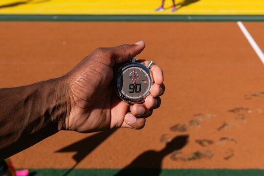 Hand of man holding stopwatch with 90 minute display on a sunny football field, with warm amber tones for sports and athletics