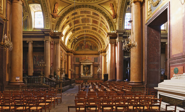 Neoclassical nave featuring columns, rows of chairs, a wooden confessional, and a large white marble cenotaph monument in Rennes Cathedral located in Brittany, France.