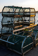 Fototapeta premium Commercial fishing and sustainable seafood industry, stack of lobster traps on a harbor pier at sunset with ocean background and golden hour light