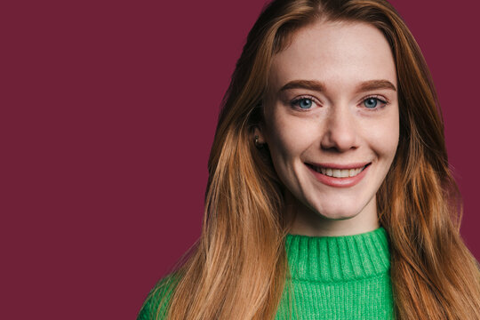 Young woman with long hair smiles against a solid colored background during a casual moment