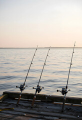 Fototapeta premium Leisure and recreation, three fishing rods set up on a wooden pier at sunset for outdoor hobby and relaxation by the calm water of a lake or river