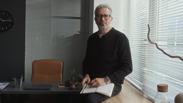 Portrait of middle aged Caucasian mental health specialist holding notebook while sitting in office and looking at camera. Footage suitable for corporate leadership and executive consulting projects