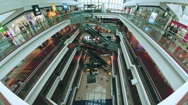 Wide angle view looking down into a modern multi-level shopping mall atrium with crisscrossing escalators, balconies and retail stores. Shopping, consumerism and urban lifestyle.