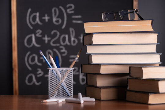 School blackboard with mathematics formulas and stack of textbooks