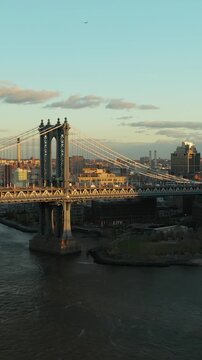 Vertical video: Forwards fly above river. View of heavy traffic on Manhattan Bridge. Slowly moving cars on upper deck and train riding under them. Brooklyn, New York City, USA