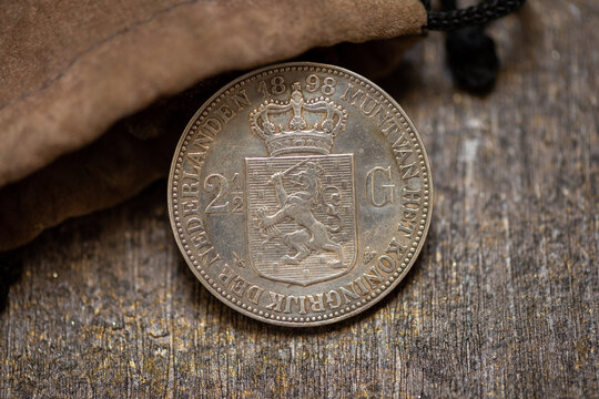 Antique dutch silver coin from 1898 in leather pouch on wooden surface. Perfect for historical, numismatic, or vintage design projects.