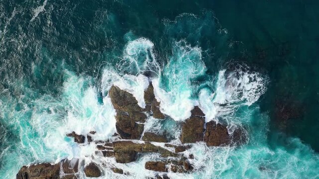 Turquoise Ocean Waves Crashing Against Dark Coastal Rocks Top View