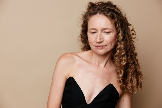 An authentic middle-aged woman with natural skin and curly hair posing against a neutral background. Concept for body positivity, self acceptance, and real beauty.