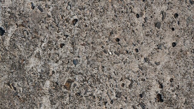 High-resolution top view of weathered gray concrete texture with visible aggregates, pebbles, and small pits, ideal for architectural backgrounds, construction designs, and industrial overlays.