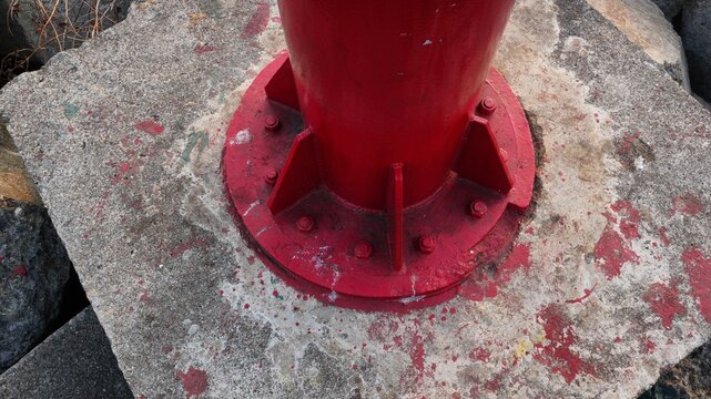 Close-up of a red metal pillar base bolted securely to a weathered concrete foundation with visible red paint stains, industrial construction detail, and structural engineering concept.