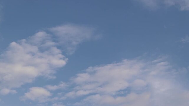 Blue sky with scattered white clouds. Minimalist natural landscape. View from below on a natural blue sky. Peaceful and calm summer sky with soft fluffy clouds floating in the morning air