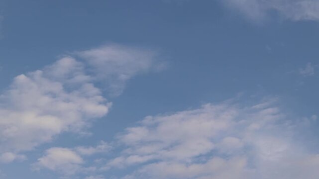 Blue sky with scattered white clouds. Minimalist natural landscape. View from below on a natural blue sky. Peaceful and calm summer sky with soft fluffy clouds floating in the morning air