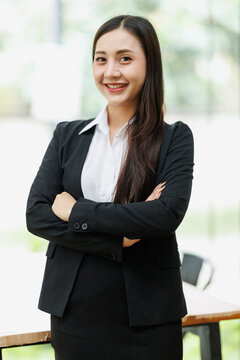 Confident asian businesswoman smiling and standing with arms crossed in a bright modern office setting, representing professional success, leadership, and determination