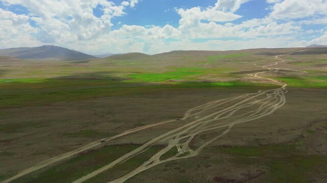 Aerial orbit shot of two 4x4 vehicles crossing paths on dirt tracks in the expansive Deosai Plains, Vast open plains with converging off road trails. Off grid expedition vehicles