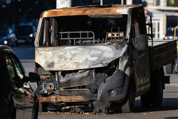 Burned small truck parked on a city street after fire front view close up © castenoid