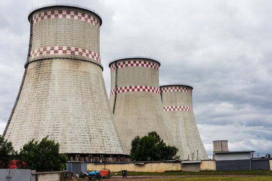 Three large industrial cooling towers with red and white patterned bands rising above power plant service buildings under cloudy sky, weathered concrete stacks in open plant grounds