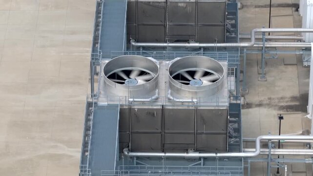 Overhead of large HVAC cooling units at a data center. Row of visible fans, metal housing and connected piping show part of the facility's cooling infrastructure, aerial forward view