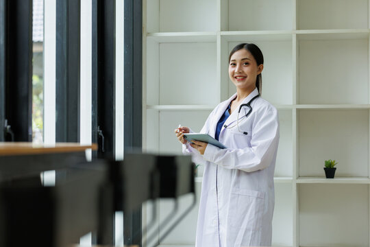 Professional female doctor smiling and holding a digital tablet with a stylus, providing modern healthcare, medical consultation, and telehealth services in a clinic or office setting
