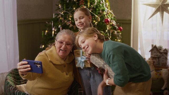Senior Caucasian woman making video call on smartphone with Caucasian boy and girl holding Christmas gifts. Footage fits holiday advertising and telecom marketing