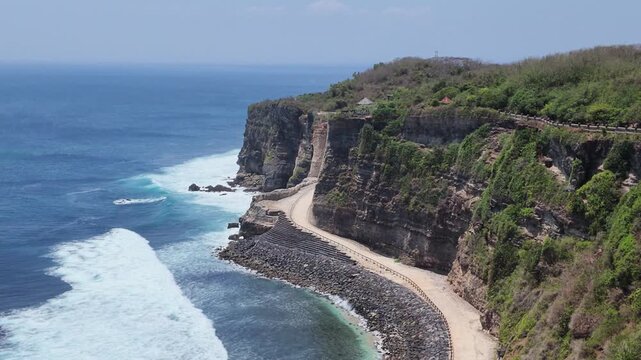 Aerial view of steep limestone cliff in Karimunjawa featuring crashing ocean waves, breakwater rocks, lush green tropical forest, exotic island coastline landscape, perfect for travel tourism